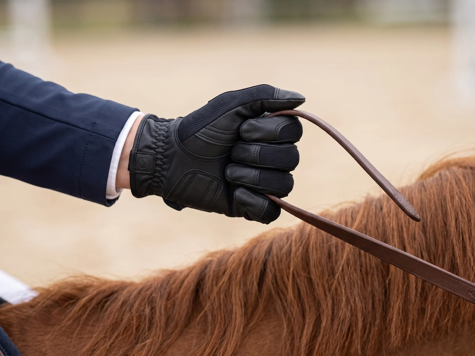 Mano con guante de piel RE-AC-01 cerrada sobre la rienda: entra entre el anular y el meñique y sale entre el pulgar y el índice