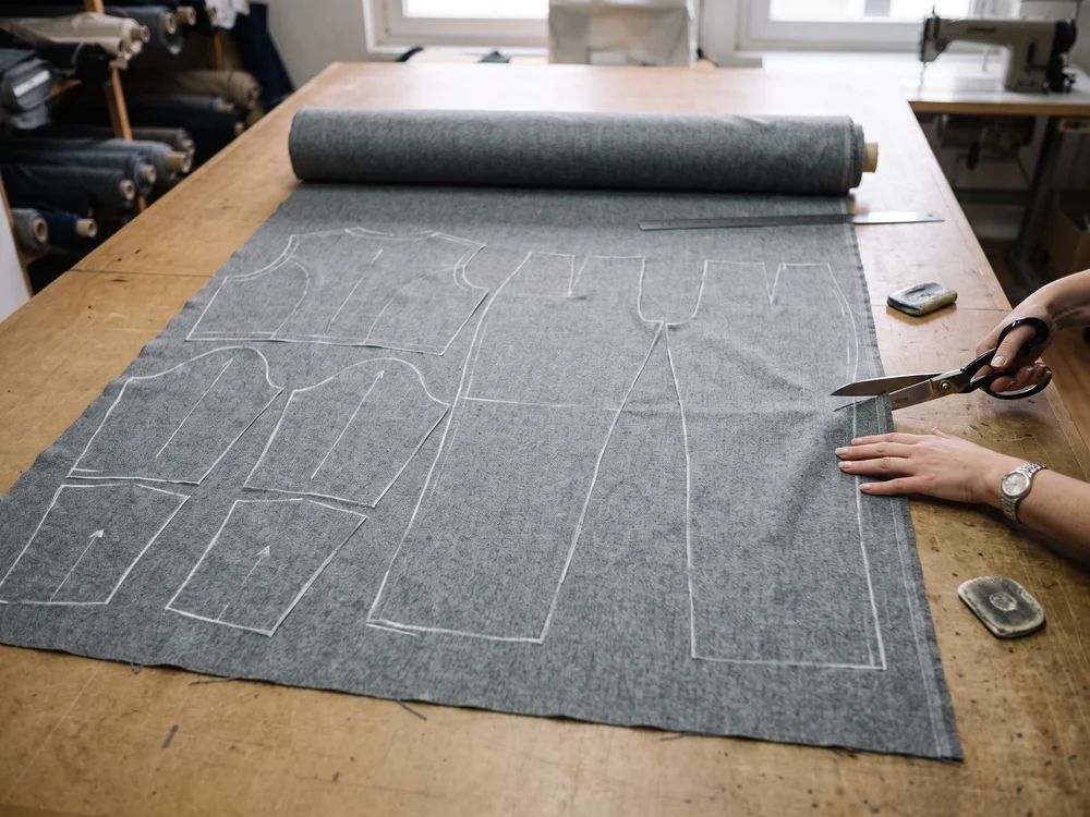 Un solo rollo de lana gris extendido con las piezas de la chaquetilla y del pantalón marcadas a tiza